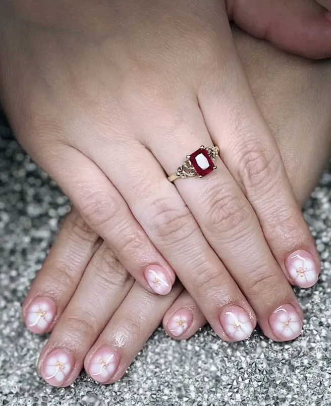 A young professional woman typing on a laptop, her hands displaying a sleek, minimalist gel manicure in soft pink. The modern workspace includes a coffee cup and notepad, emphasizing style and productivity.