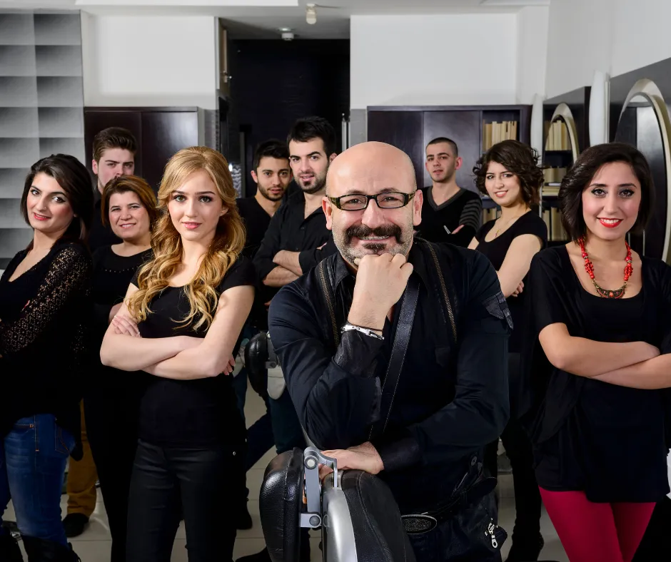 Salon team showing a mixed group of male and female professionals dressed in black clothing. Salon venue backdrop with black walls, shelving and mirrors. Representative of the salon industry written for by Salonpreneur Magazine.