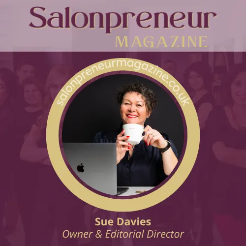 Sue Davies, Founder & Editorial Director of Salonpreneur Magazine. Sue wears black shirt, and holds white cup in both hands wearing red nail polish. Dark hair, minimal make up with red lipstick. Sitting desk facing camera with open laptop. Subscribe at  www.salonpreneurmagazine.co.uk