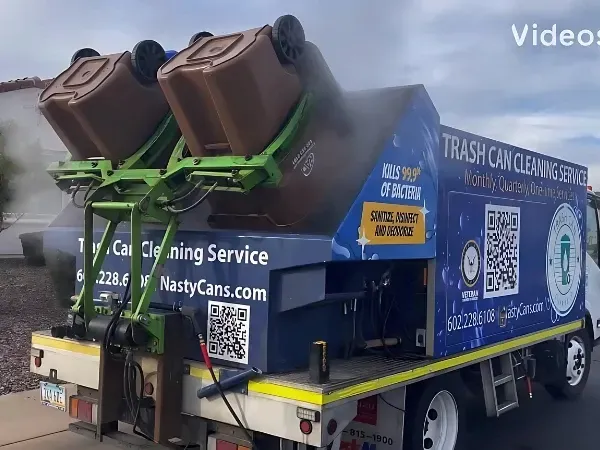 A trash can cleaning truck lifting and sanitizing two brown garbage bins, with steam rising as they are disinfected.