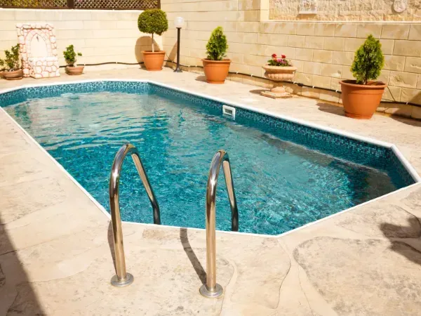 Geometric swimming pool with a metal ladder, surrounded by stone paving and potted plants.