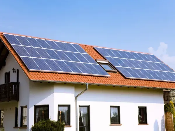 Solar panels installed on a metal roof, surrounded by green trees, providing sustainable energy for the home.