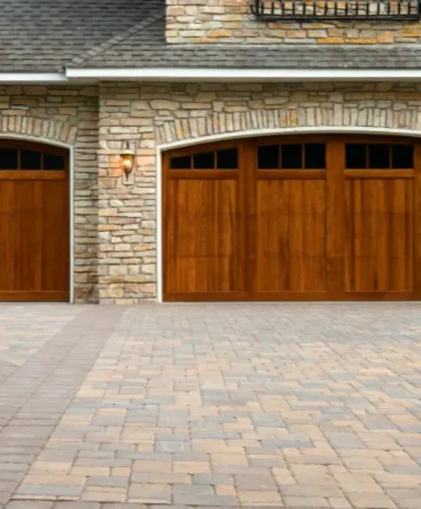 Modern stone house exterior with wooden garage doors and brick driveway