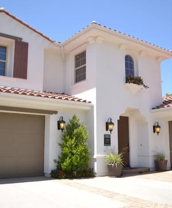 White Mediterranean-style home with terracotta roof tiles, arched entryway, and potted plants.