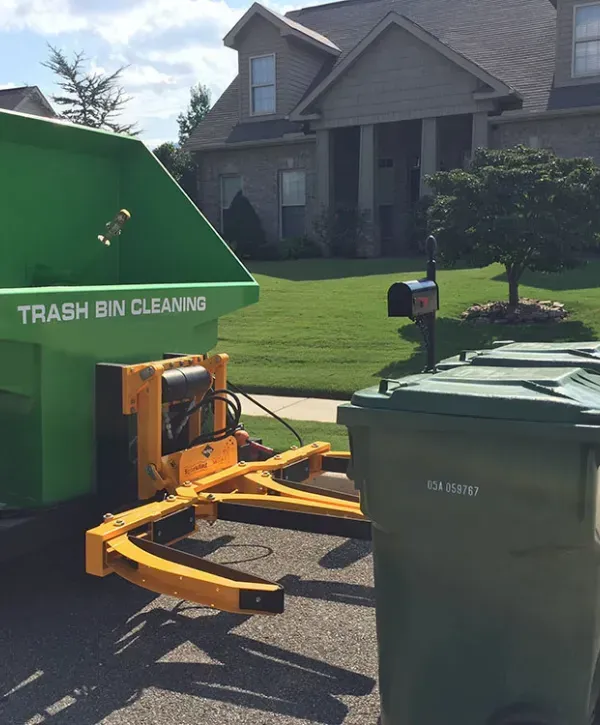 Trash bin cleaning service truck with green bins outside residential home 