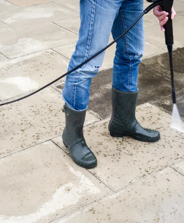 Person pressure washing outdoor stone patio wearing boots and jeans