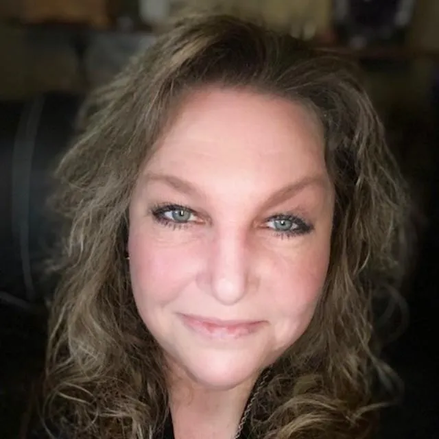 Close-up headshot of a smiling woman with long, curly blonde hair and blue eyes