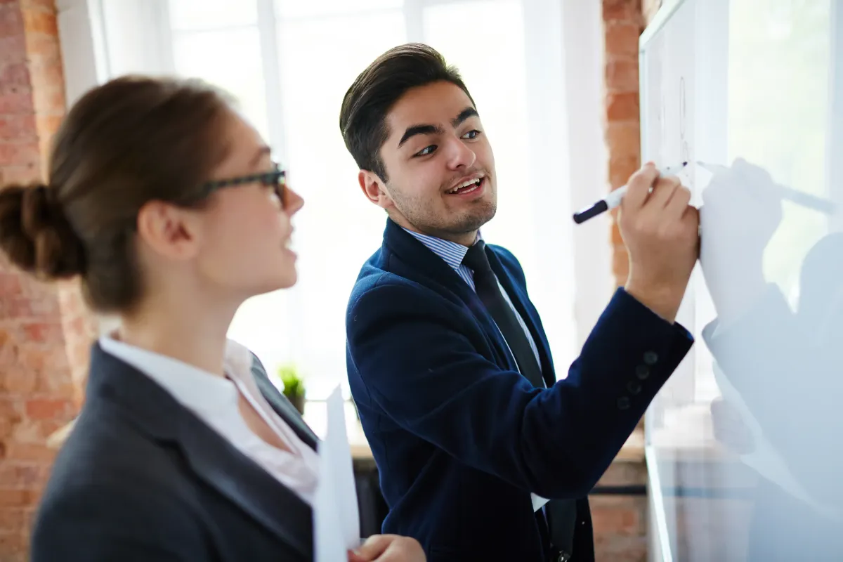 Business coach guiding a client through a strategy session at a whiteboard, supporting leadership development and skill building.
