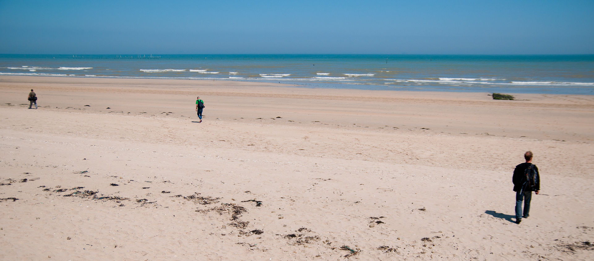 Wide sandy Utah Beach in Normandy, France with a few people walking along the shoreline under a clear sky, illustrating a quiet landscape with historic significance.