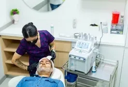 A woman in medical clothing applies a facial mask to a man's face in an indoor healthcare setting, surrounded by medical equipment and supplies.