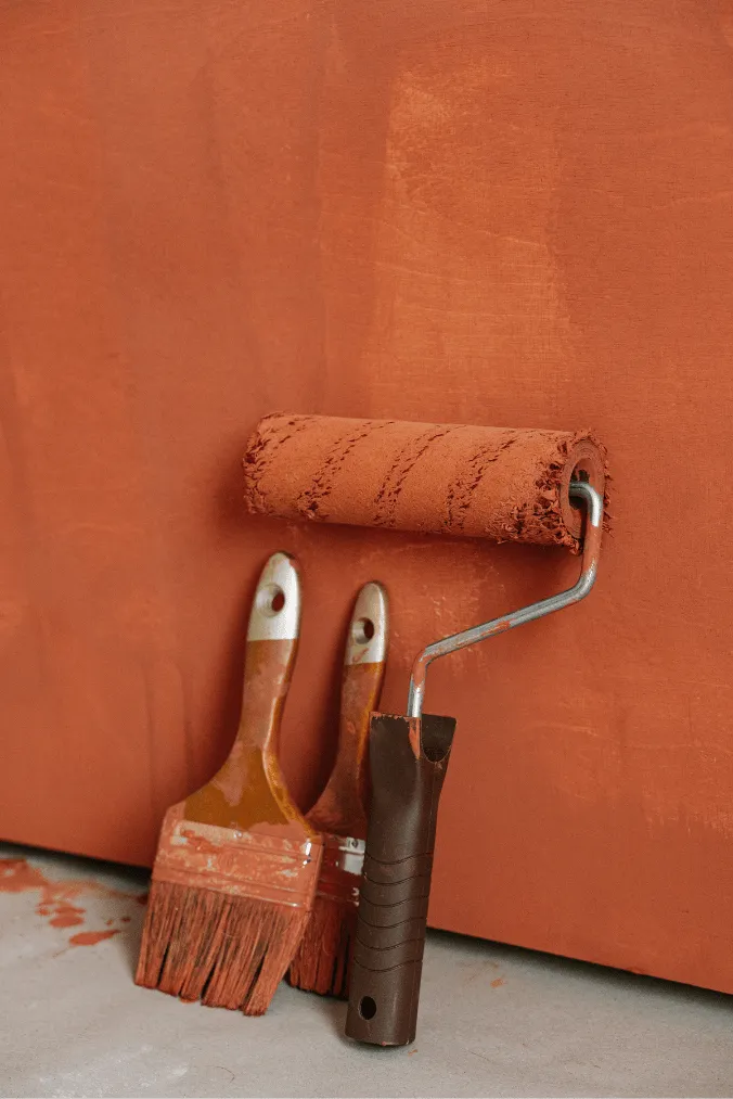 Verfroller en kwasten bij een terracotta geschilderde muur tijdens schilderwerken door LevelUp Renovaties