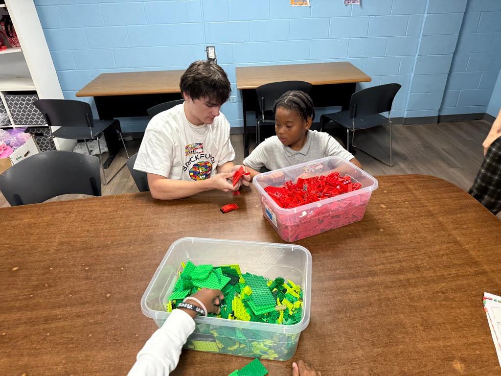 Two Brick Fusion participants building together with red LEGO bricks