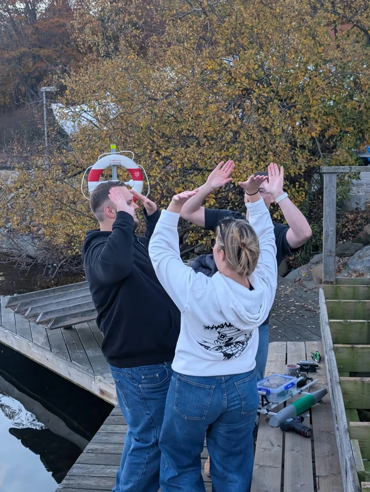 A single-seat, sponsor-covered experimental boat from the Monaco Energy Boat Challenge moves across deep blue water, piloted by a person in an orange life vest and bright yellow helmet, with an Italian flag flying from a thin mast and a concrete harbor wall and a few distant spectators in the background.