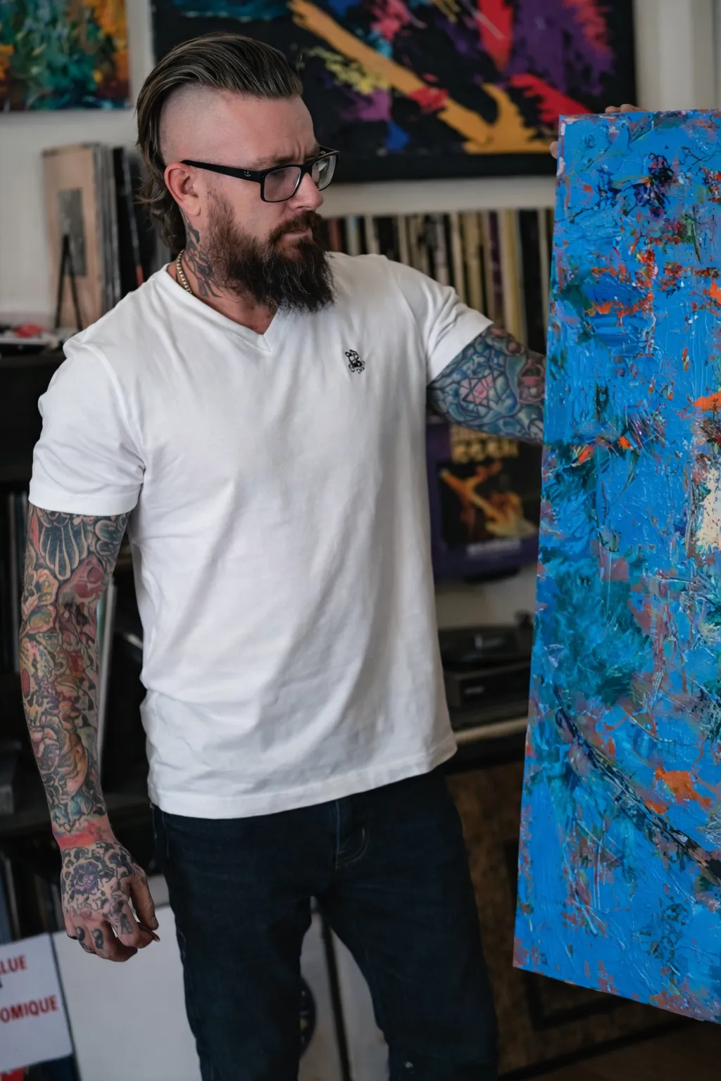 Portrait of Daniel Drake, a bearded man in his 30s with thoughtful expression, wearing a charcoal shirt, standing in a softly lit studio with canvases in the background.