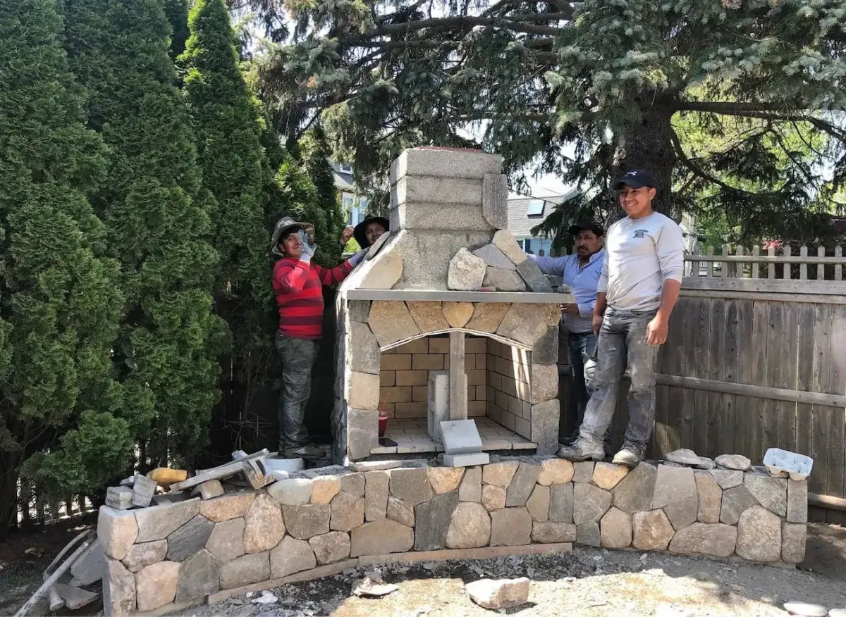 Nash & Brown Masonry crew building a custom natural stone outdoor fireplace and masonry wall in Marblehead, MA.