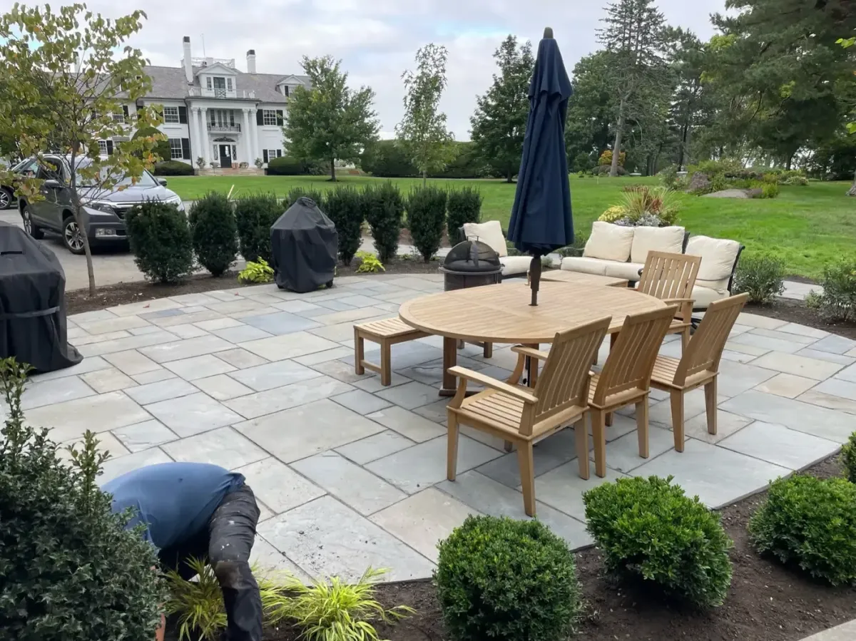 Custom bluestone patio installation with outdoor dining area and professional landscaping in Marblehead, MA by Nash & Brown Masonry.