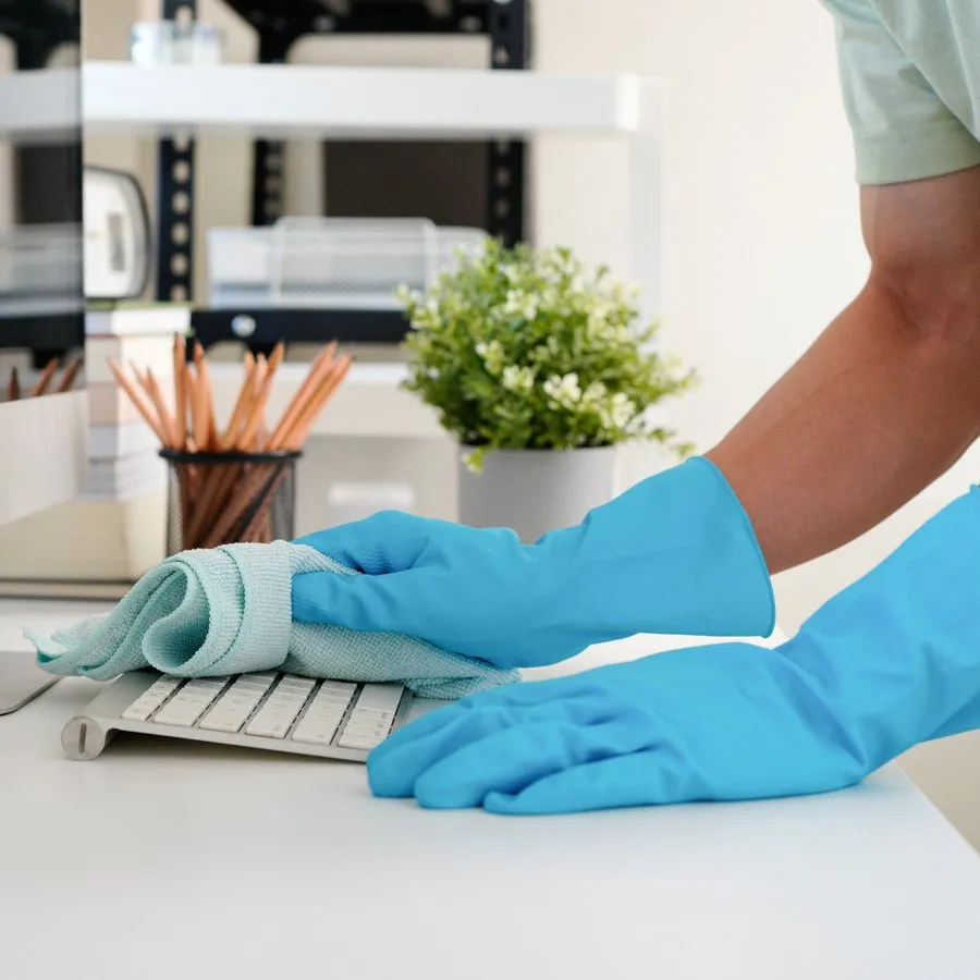 Nicholas Barnes Cleaning Services technician in blue gloves sanitizing a computer keyboard and workstation