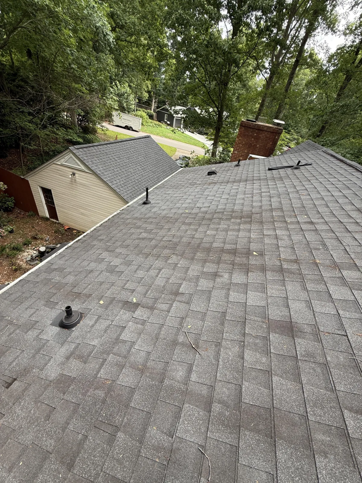 High-angle view of a shingled roof slope with plumbing vents and a brick chimney