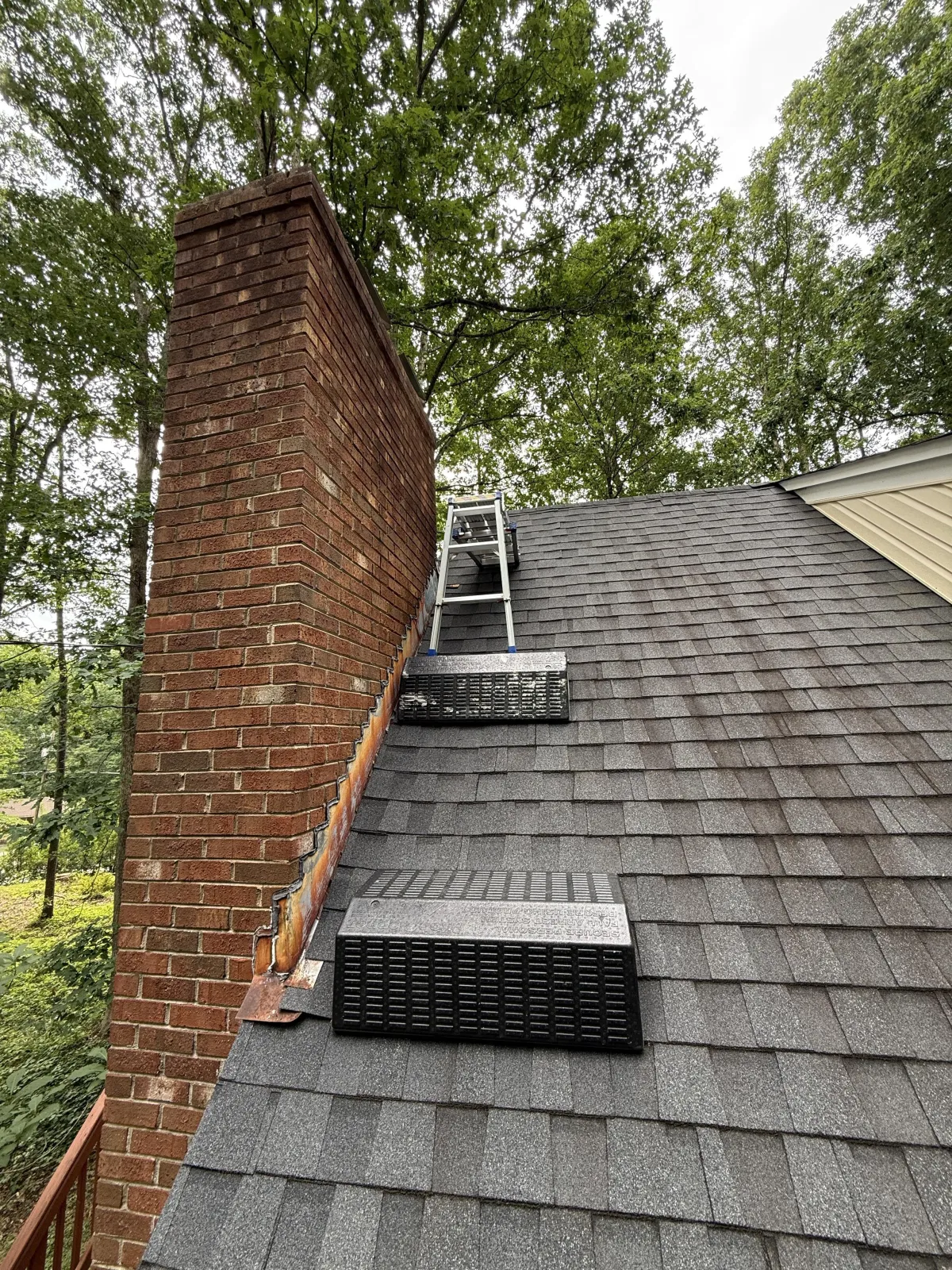 Exterior view of a brick chimney with metal step flashing along an asphalt shingle roof