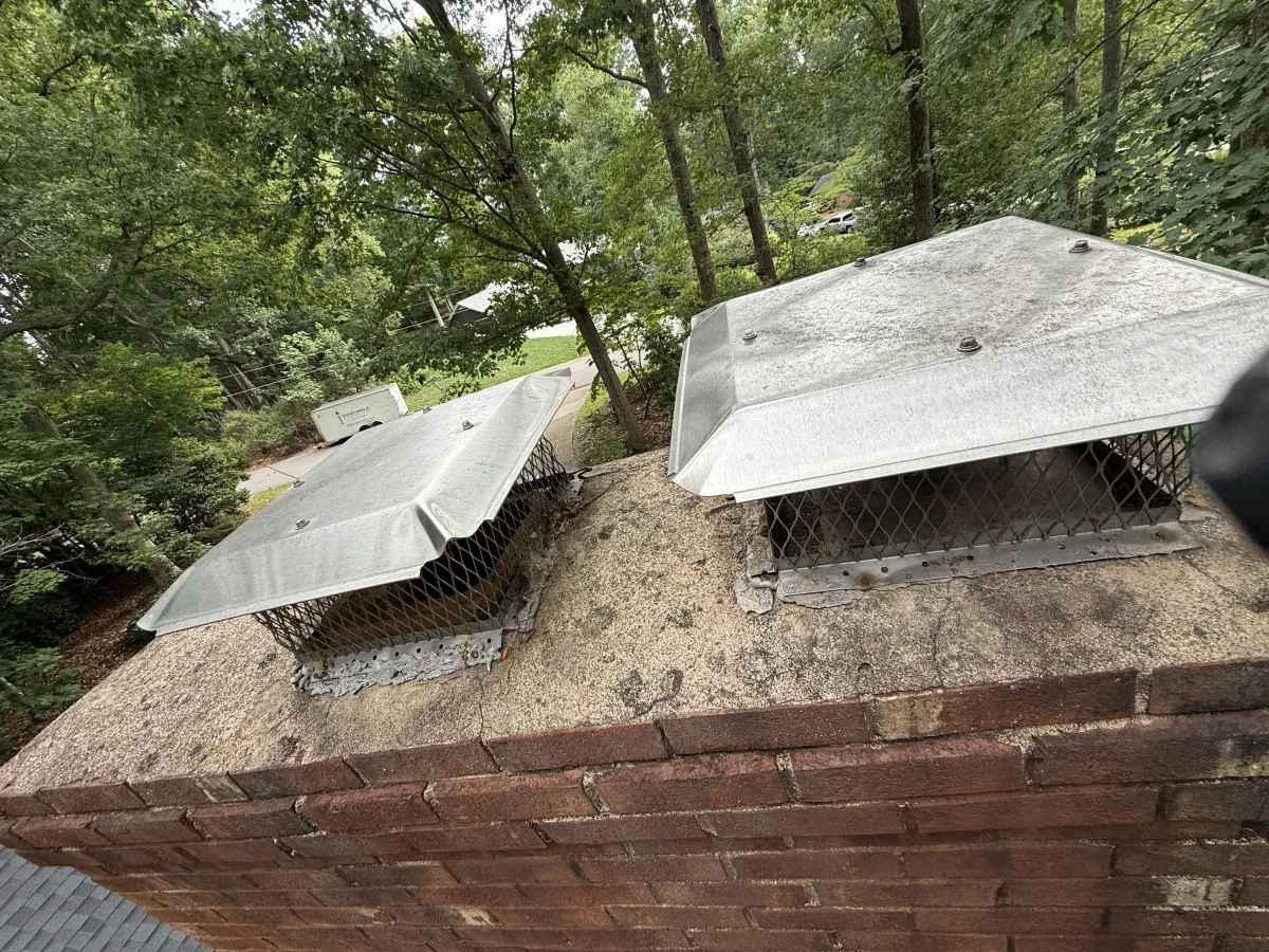 High-angle view of two metal chimney flue caps installed on a concrete crown over a brick chimney