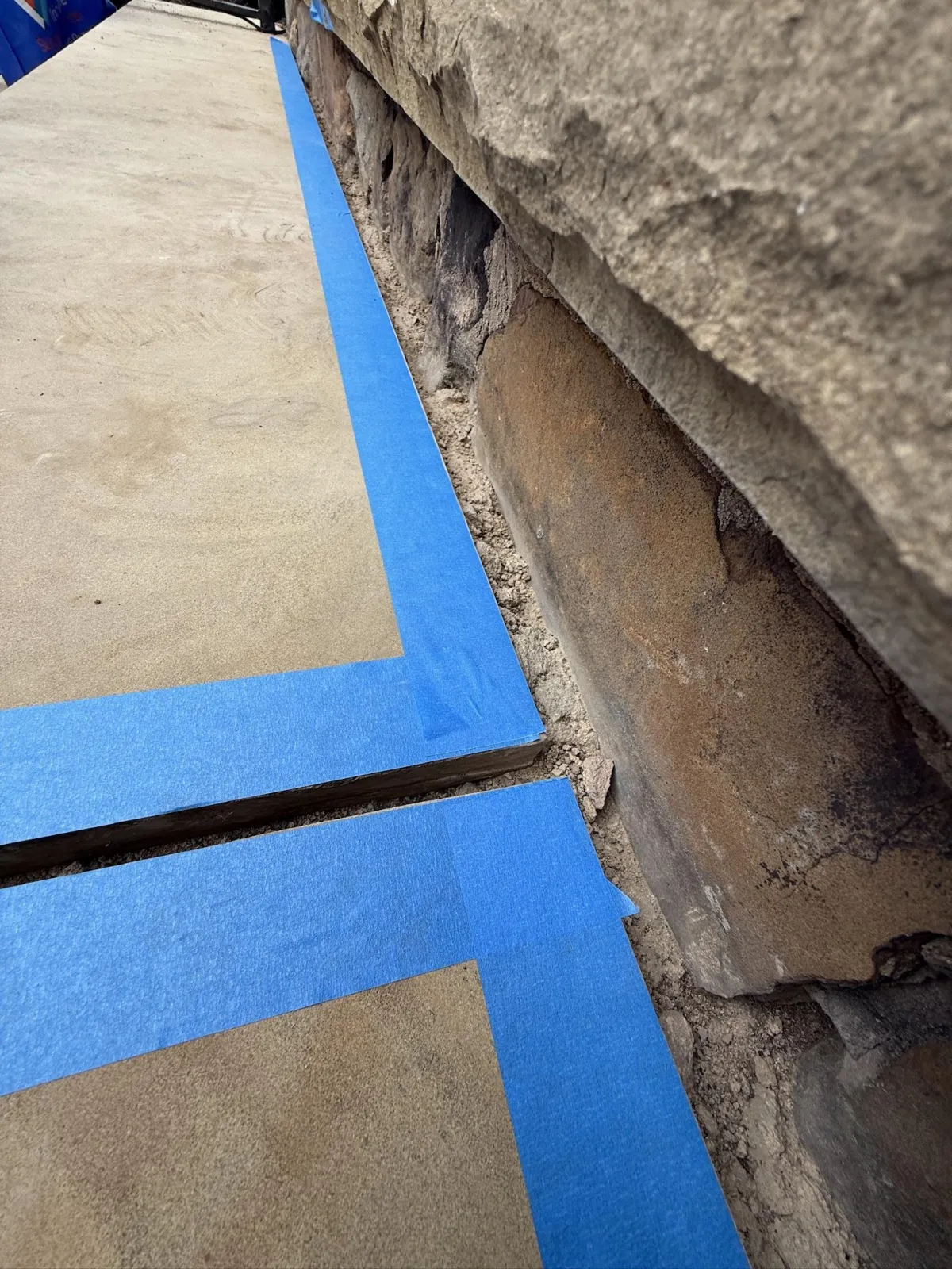 Close-up of blue painter's tape applied along the edges of stone step joints and base