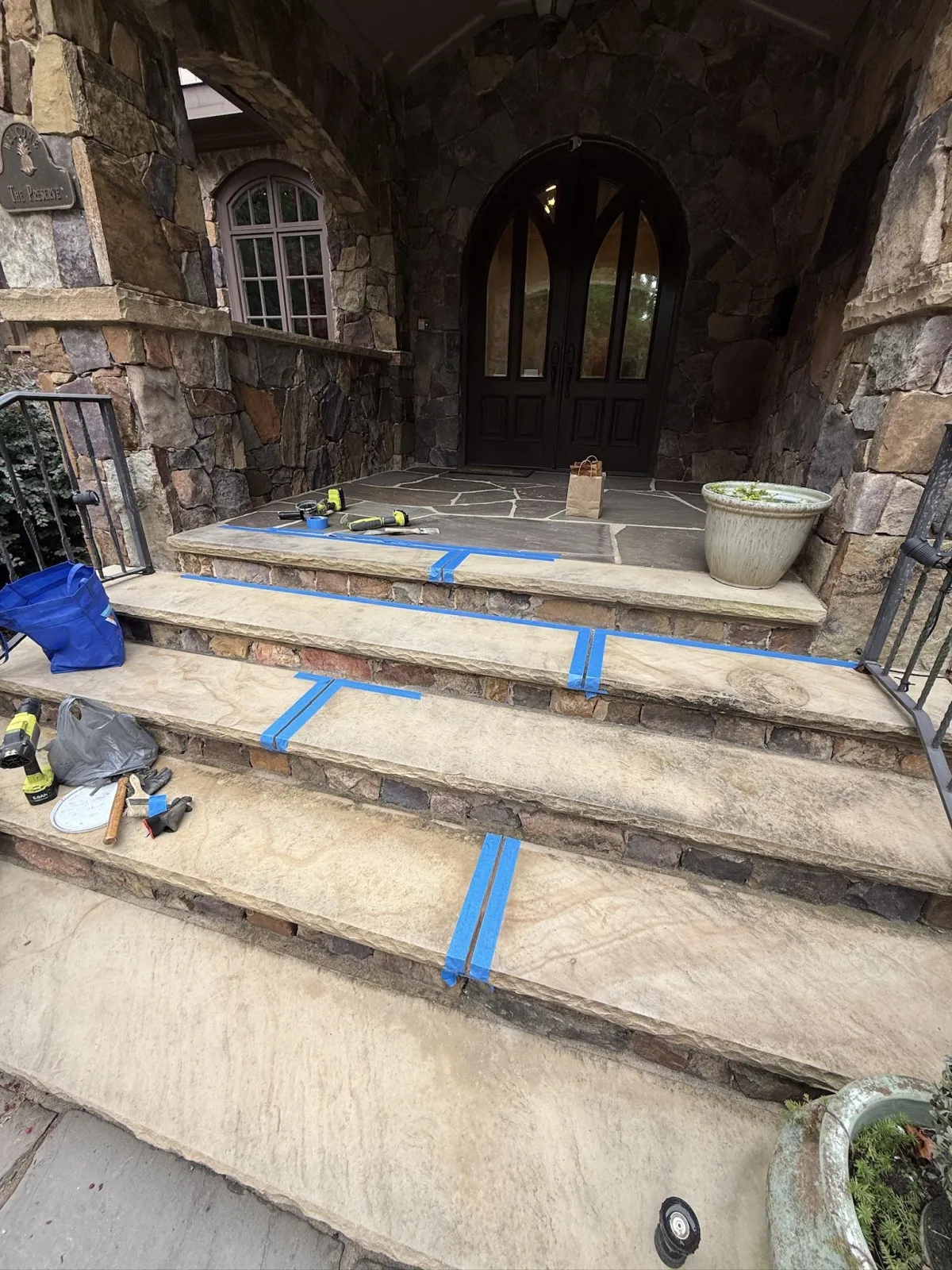 Stone steps leading up to a grand entryway, with blue painter's tape applied to the joints and tools resting on the steps and landing.