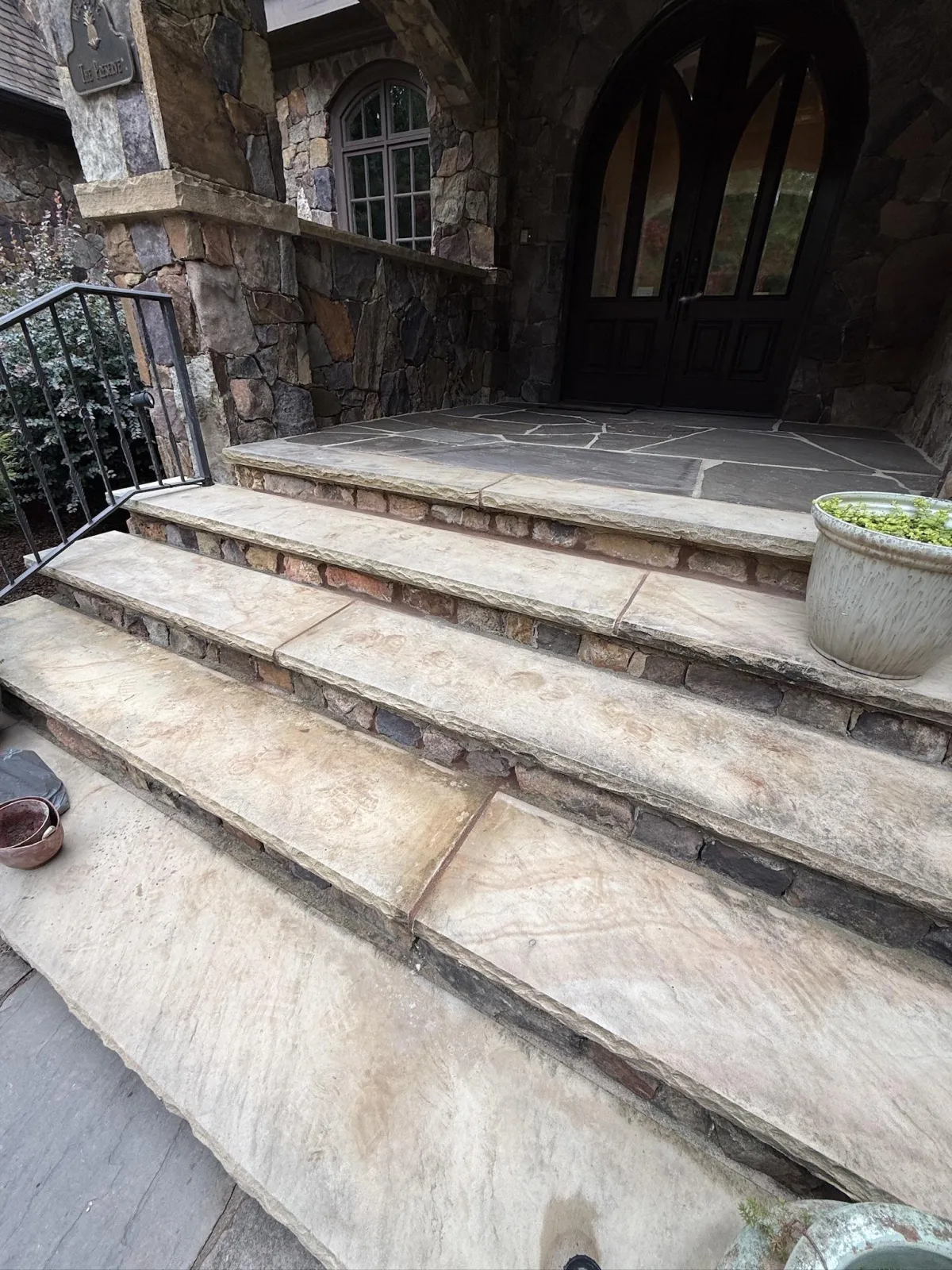 Clean stone steps leading up to a grand entryway with a dark arched door and stoned facade