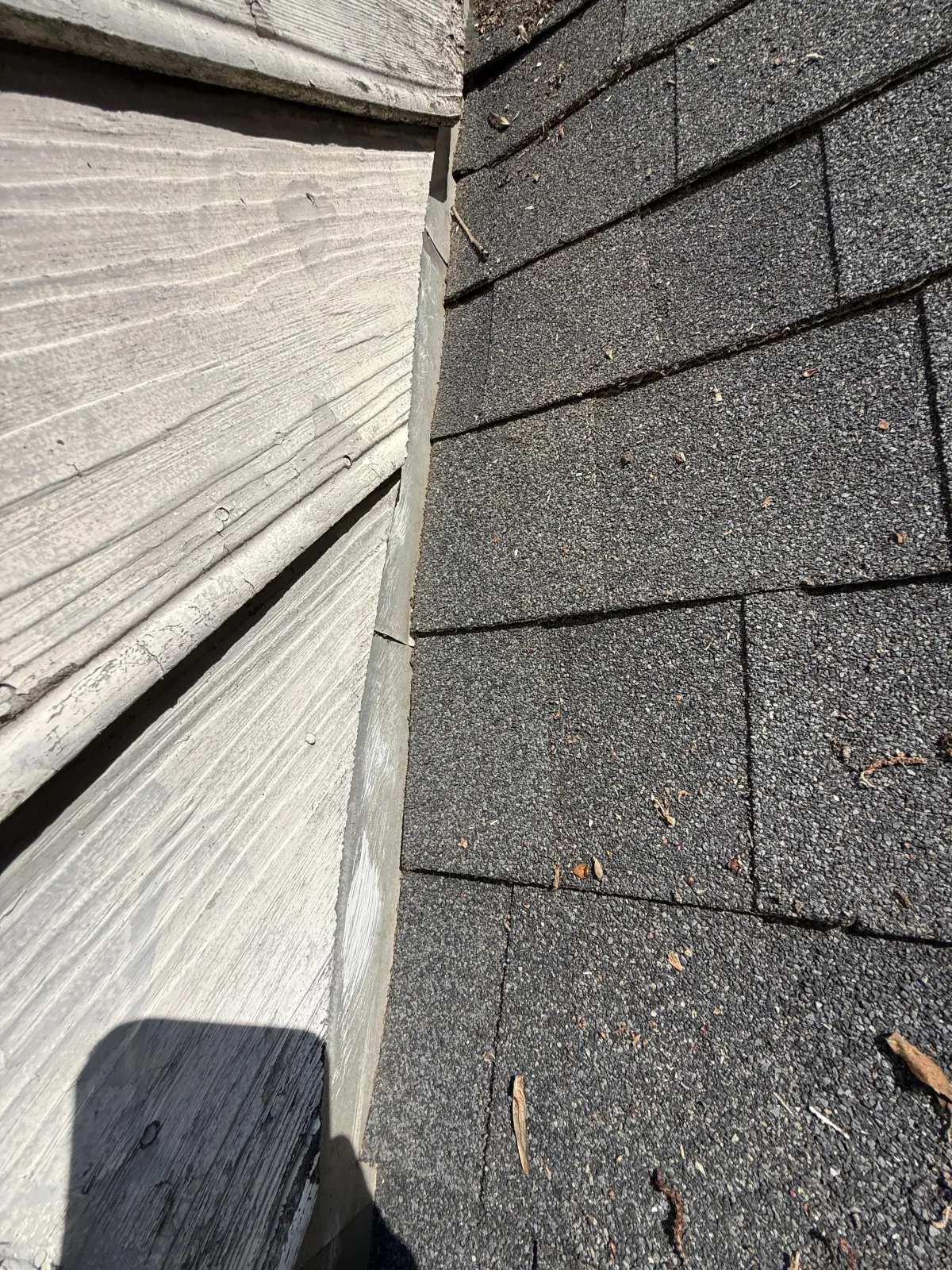 Close-up of metal step flashing installed along the intersection of a shingled roof and vertical siding.