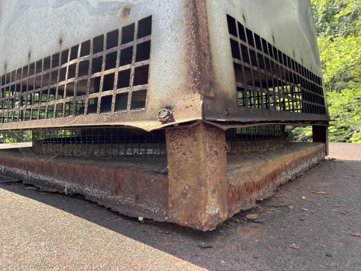 Close-up of heavy rust and corrosion on a rooftop ventilation housing unit and curb base.