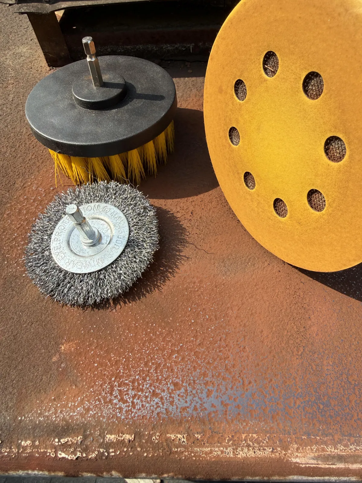 Close-up of rotary tool attachments and a sanding pad on a rusted metal surface.
