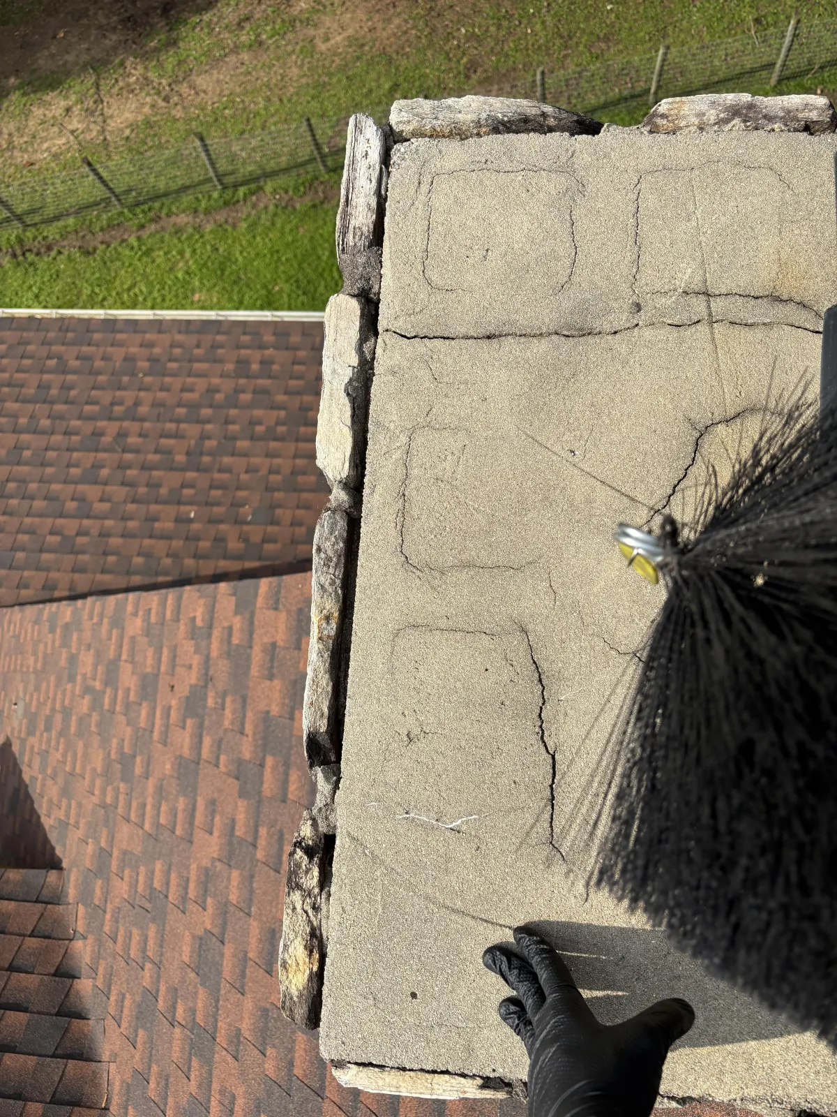 Hig-angle view of a concrete chimney crown covered with a silver-gray waterproof coating next to a black cap.