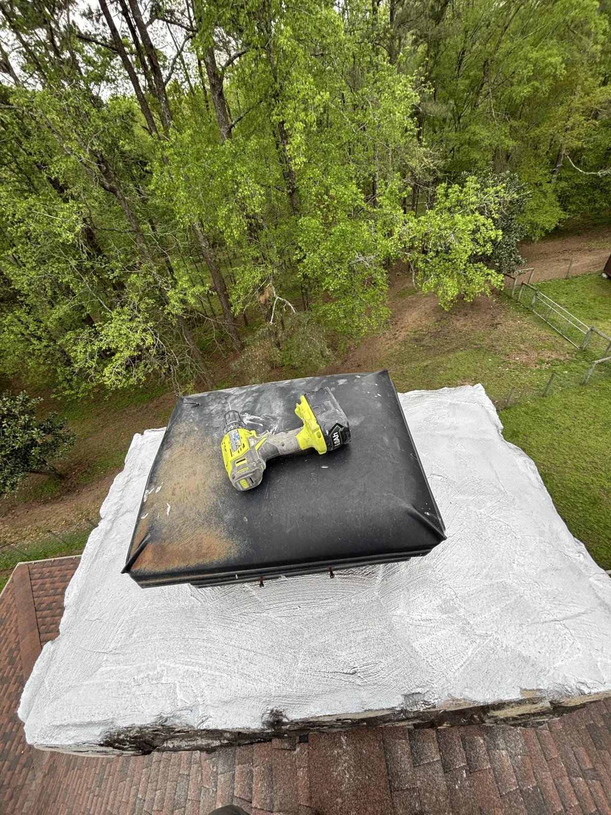High-angle view of a concrete chimney crown covered with a silver-gray waterproof coating next to a black cap.