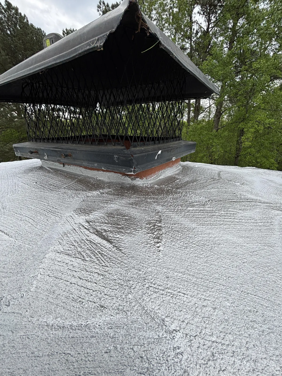 High-angle view of a concrete chimney crown covered with a silver-gray waterproof coating next to a black cap.