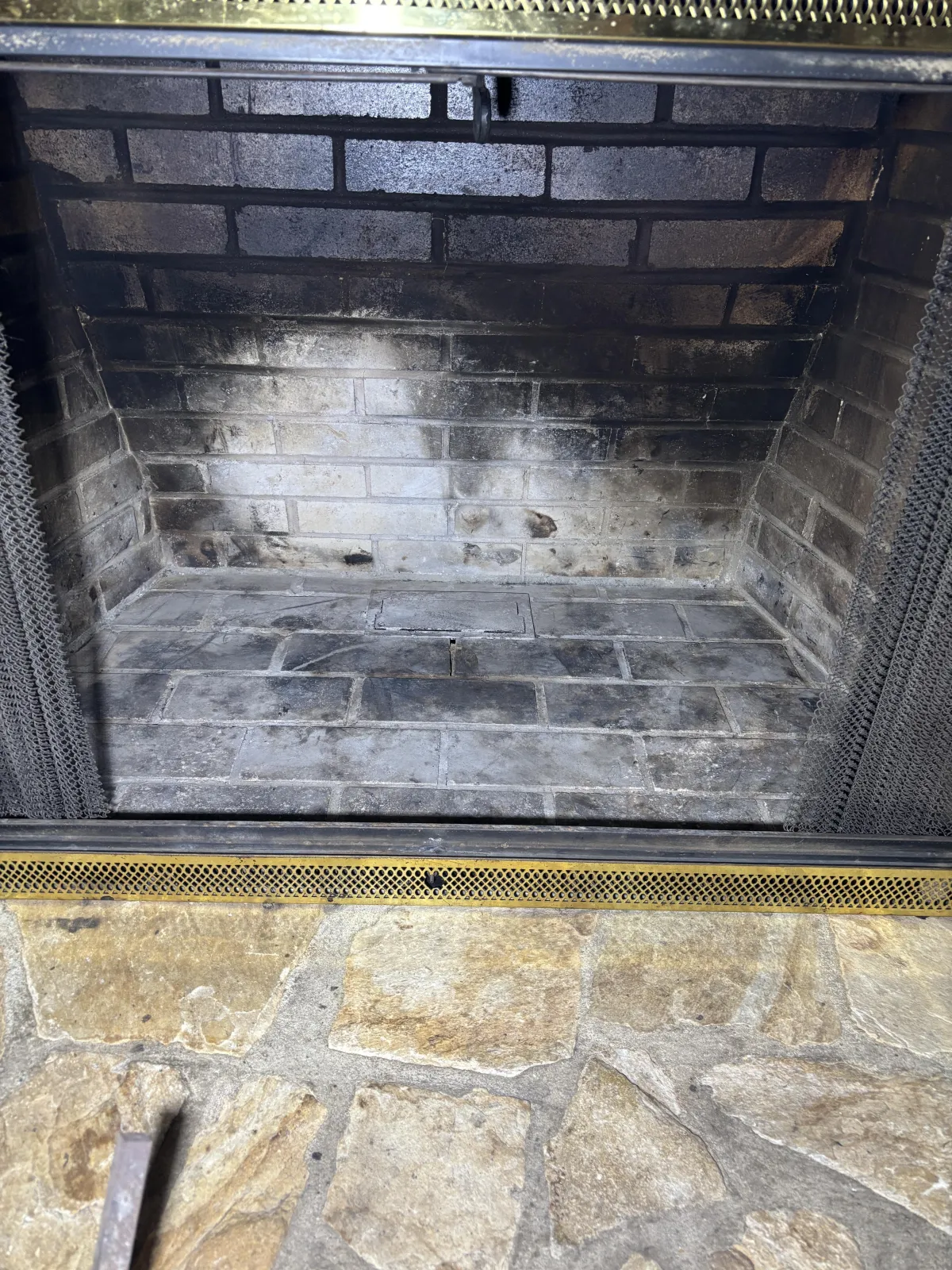 Close-up of grey ash and soot accumulation surrounding a metal grate inside a fireplace hearth