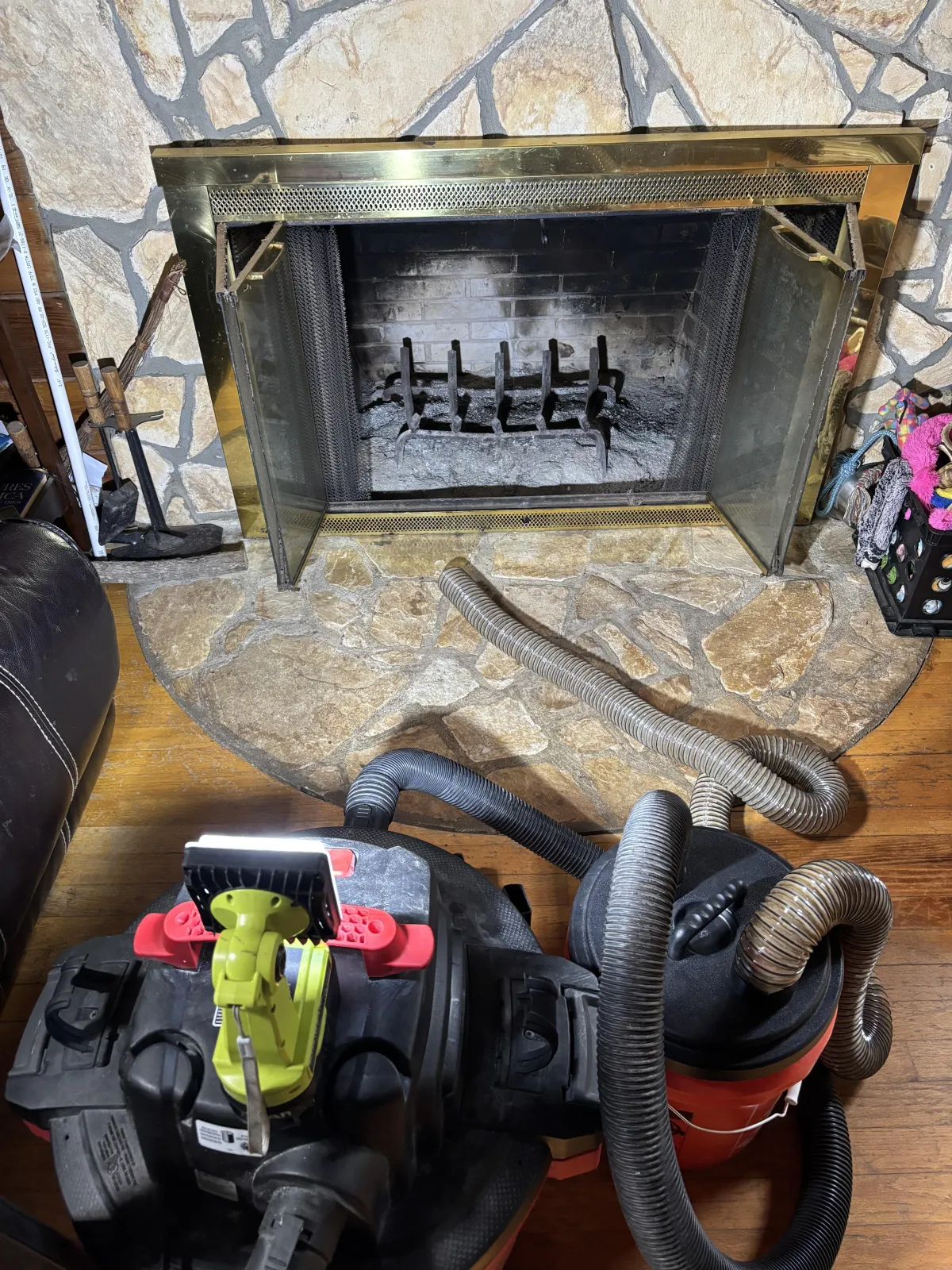 Setup of shop vacuums and hoses on a wood floor in front of a stone fireplace hearth and brass frame.