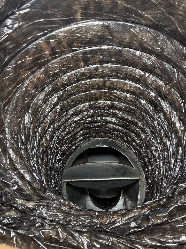 Interior view looking through a flexible HVAC duct at a closed metal damper valve.