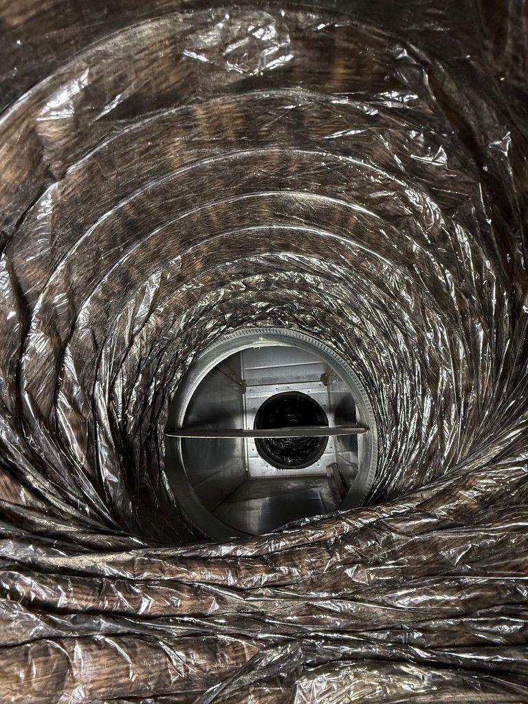 Interior view looking through a flexible HVAC duct at a metal connection collar and open damper valve.