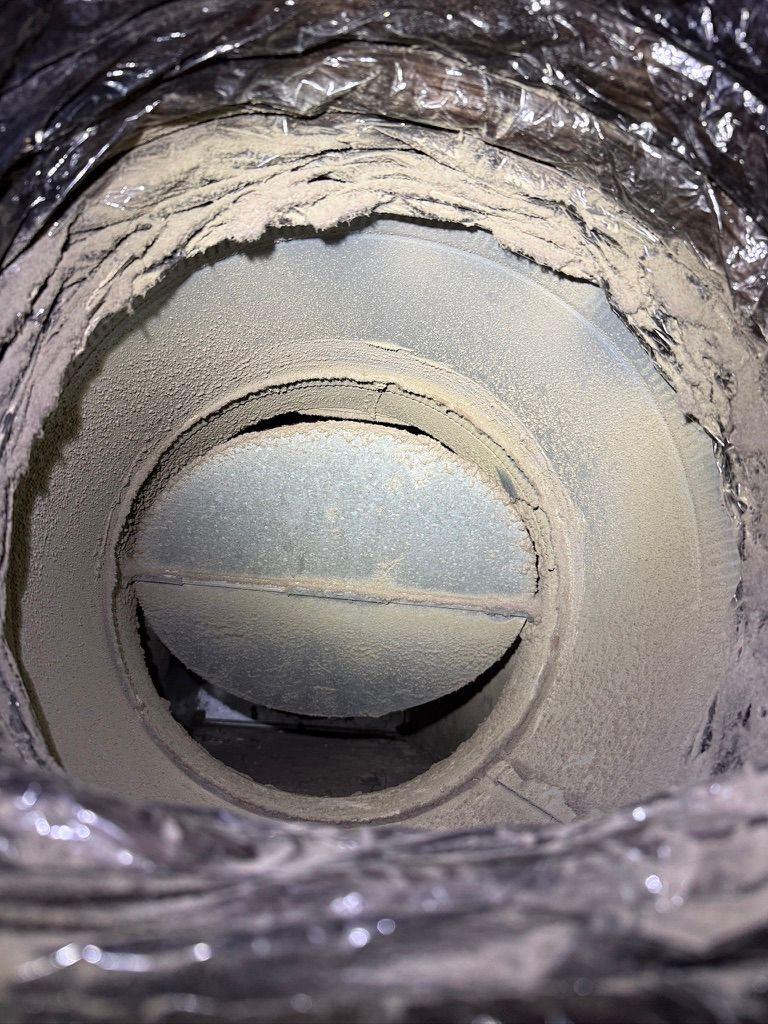 Close-up interior view of severe dust and debris caked inside an HVAC duct damper.