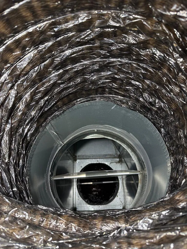 Interior view looking through a flexible HVAC duct at a clean metal collar and open damper valve.