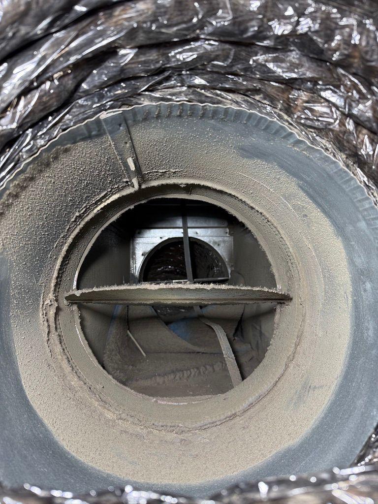 Close-up view of heavy dust and debris buildup inside a flexible HVAC duct damper valve.