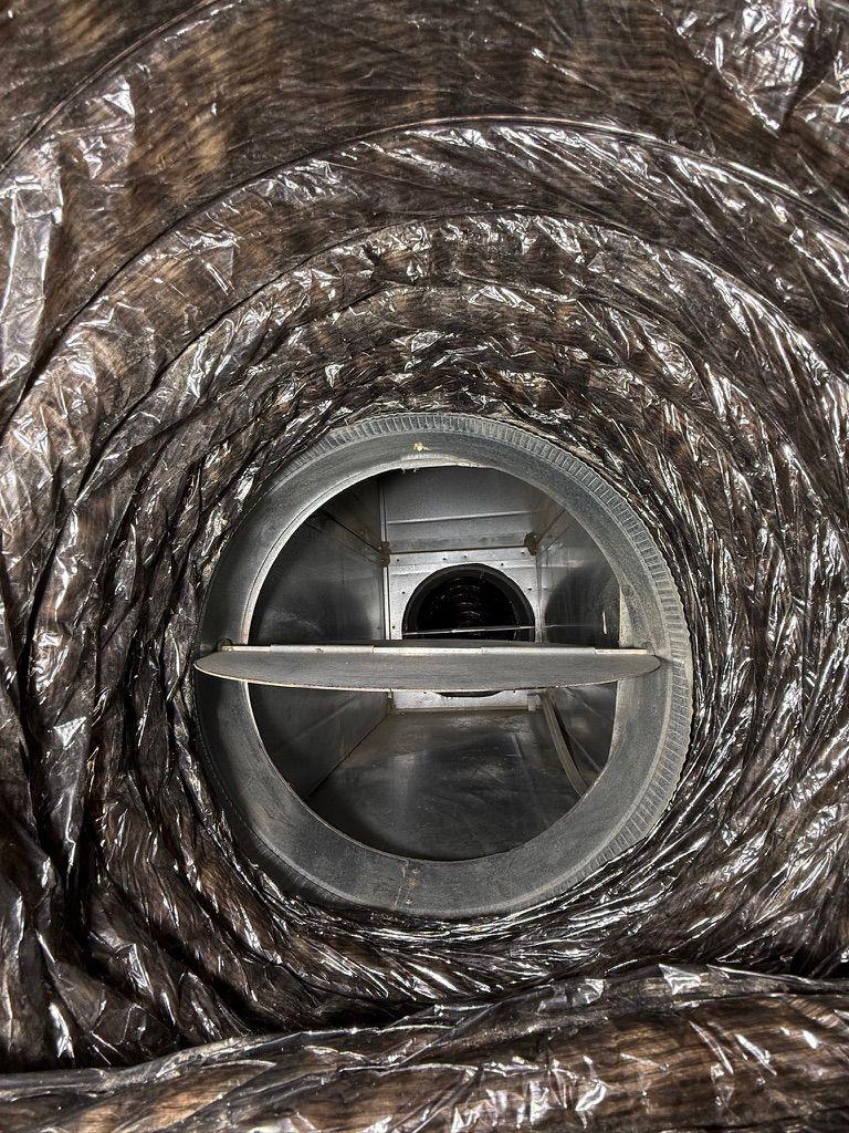 Interior view looking through a flexible HVAC duct at a round metal damper valve mechanism