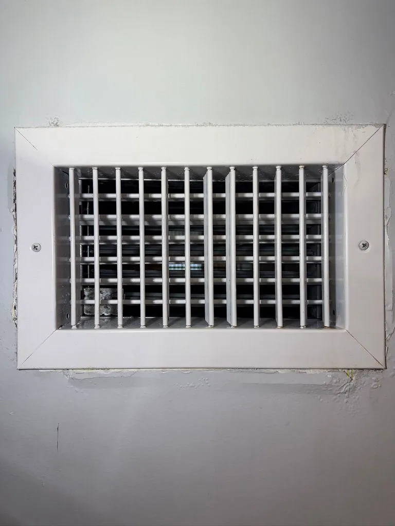 Close-up view of a clean white HVAC wall supply air register vent with adjustable vertical and horizontal louvers, mounted securely on a painted wall.