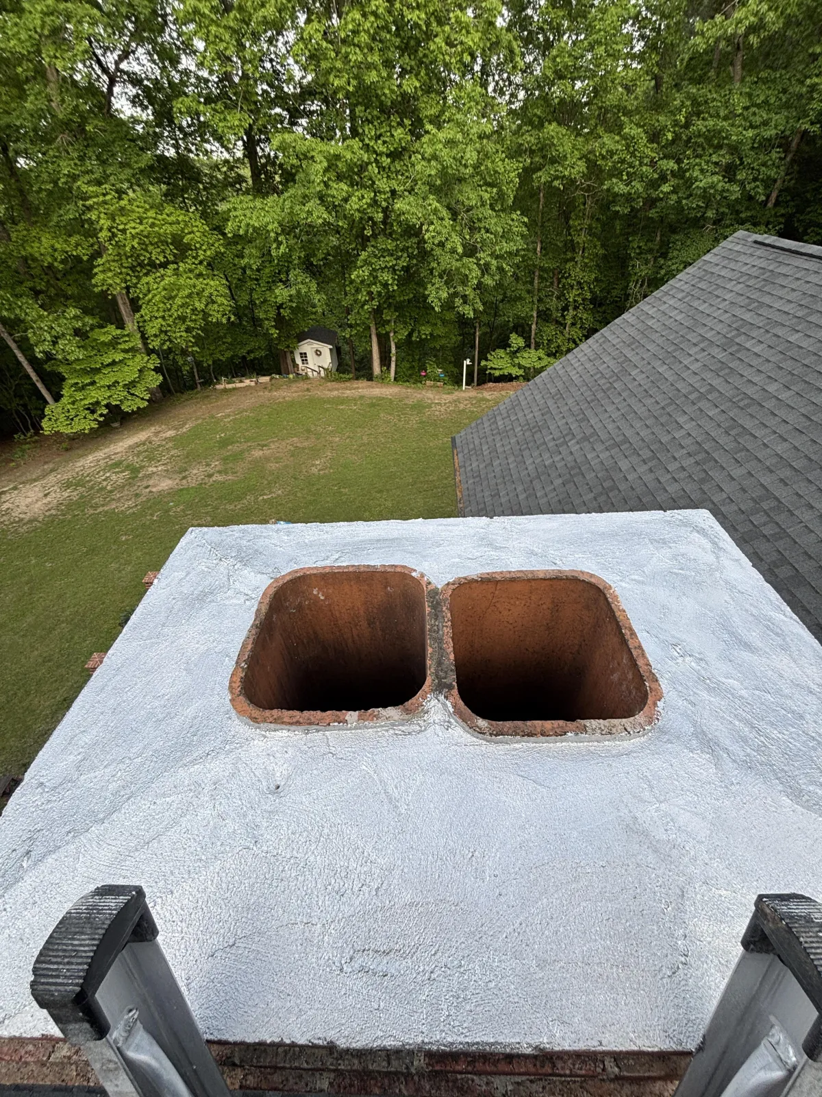 High-angle inspection view of a double-flue chimney with a sealed concrete crown and silver-gray waterproof coating