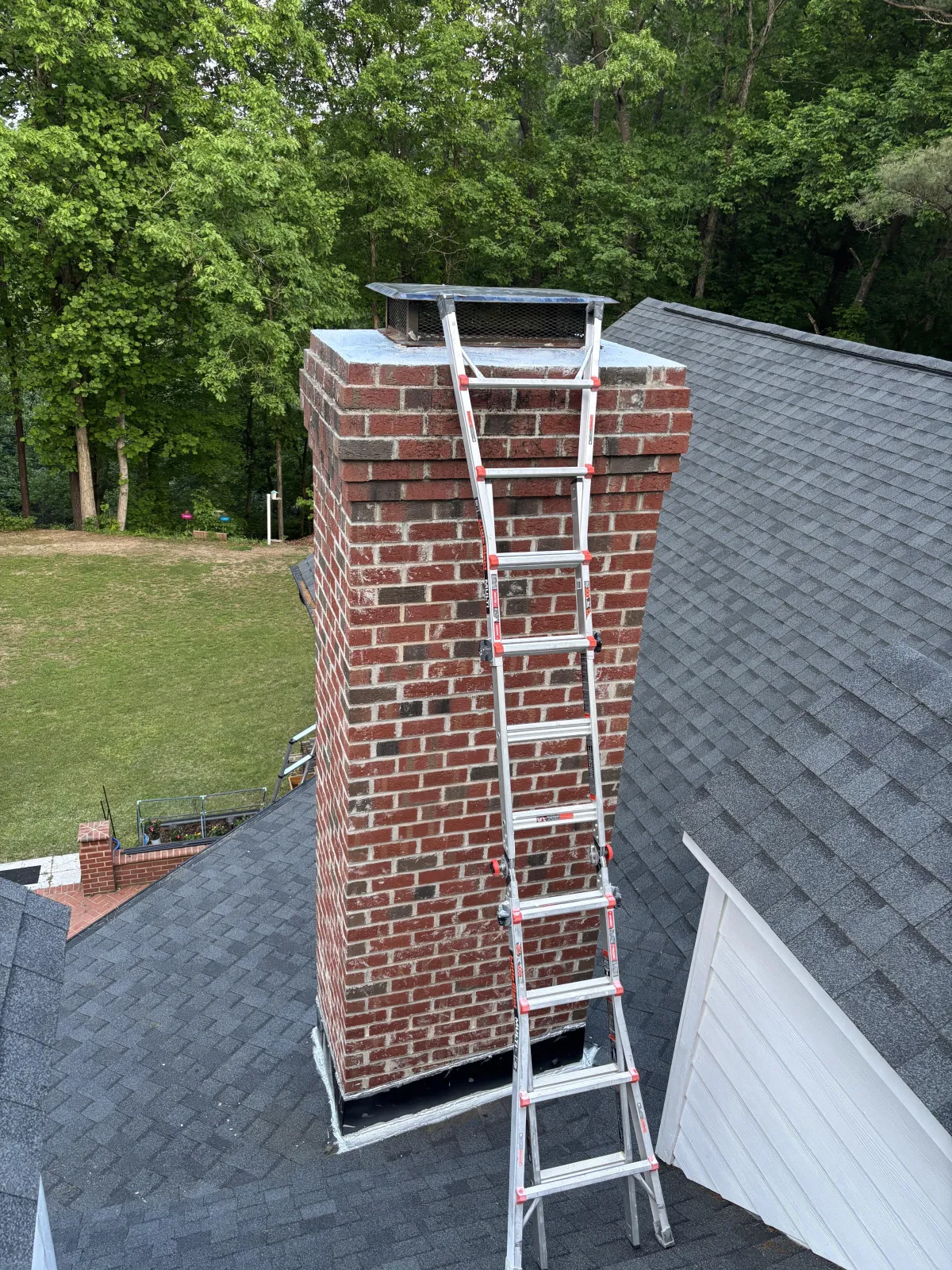 High-angle view of an extension ladder propped against a brick chimney on a shingled roof.