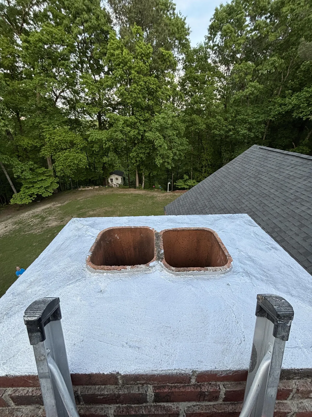 High-angle view of a sealed double-flue chimney crown with a silver-gray waterproof coating
