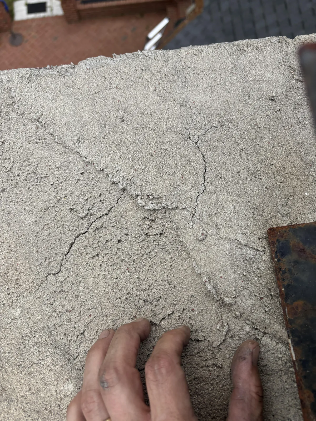 Close-up of a damaged concrete chimney crown showing surface cracks and a gloved hand inspecting the wear.