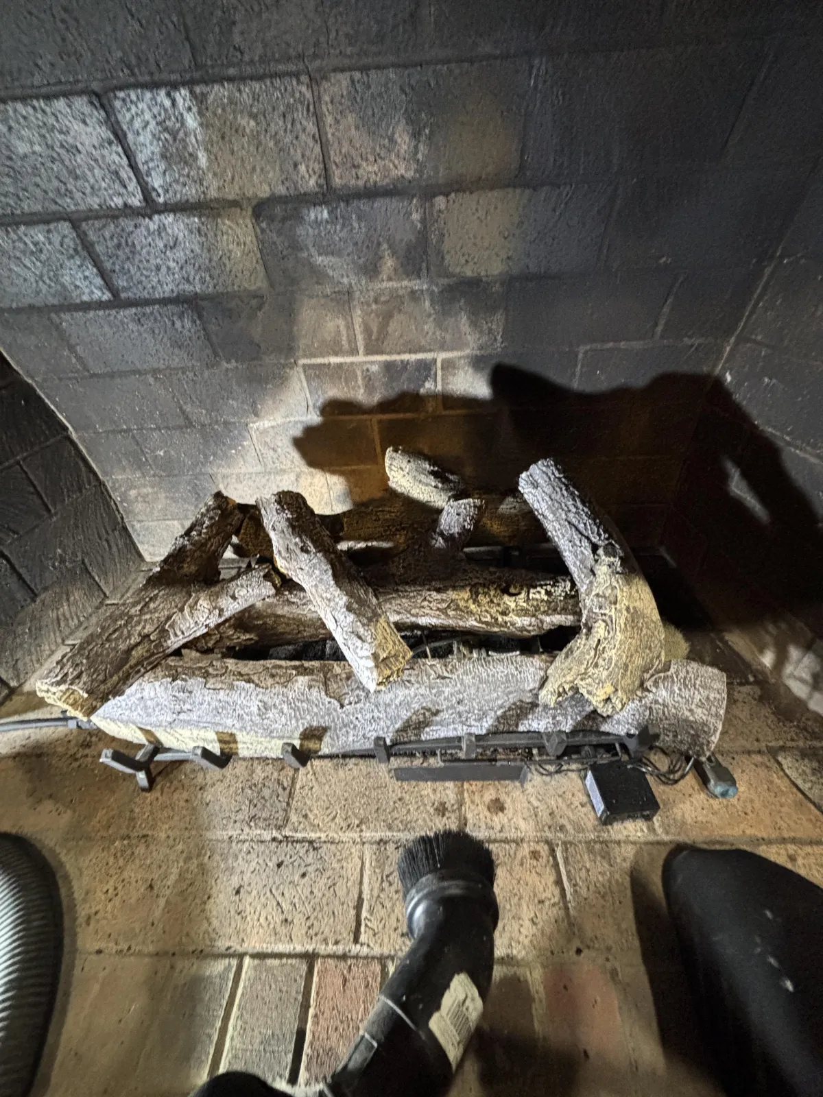 Interior view of a brick fireplace with a log on a grate and a vacuum hose on the hearth.