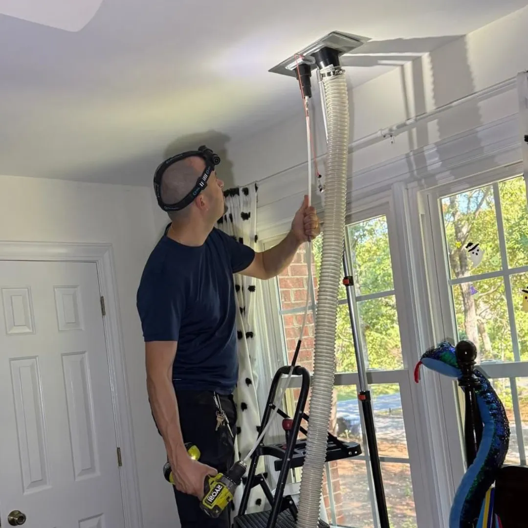 Professional technician cleaning indoor ceiling dryer vent hose with vacuum equipment.