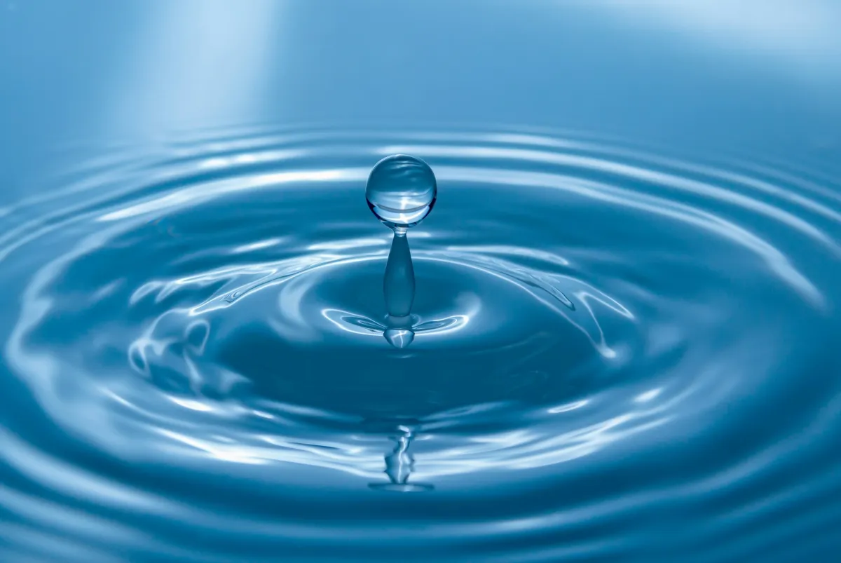 a gradient blue coloured image of a water droplet as it bounces back out with the ripple rings around it.