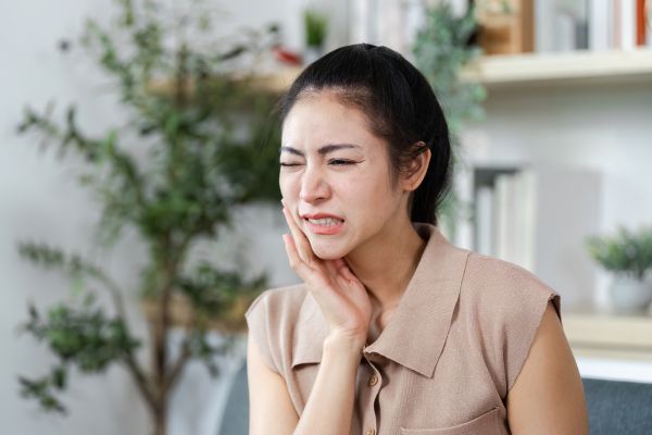 Asian lady holding her jaw grimacing.